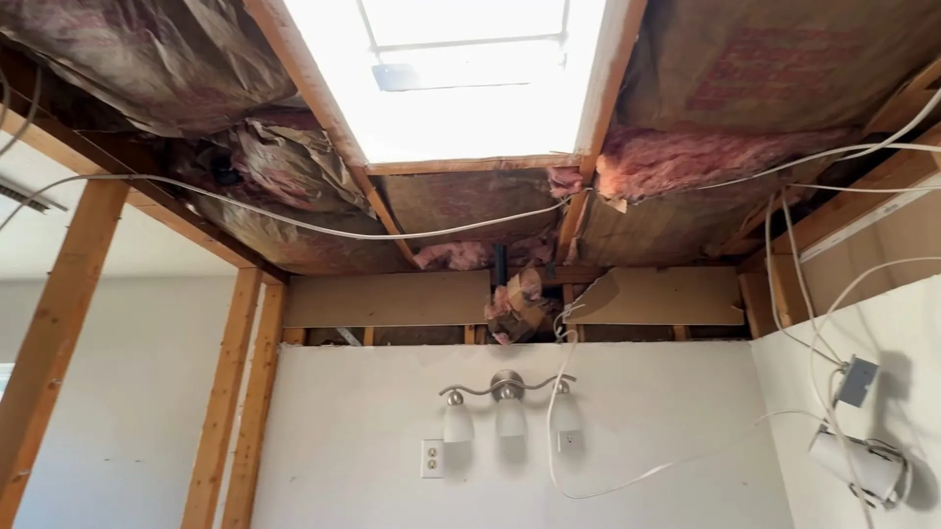 Bathroom ceiling opened to the joists with insulation hanging and a light fixture below