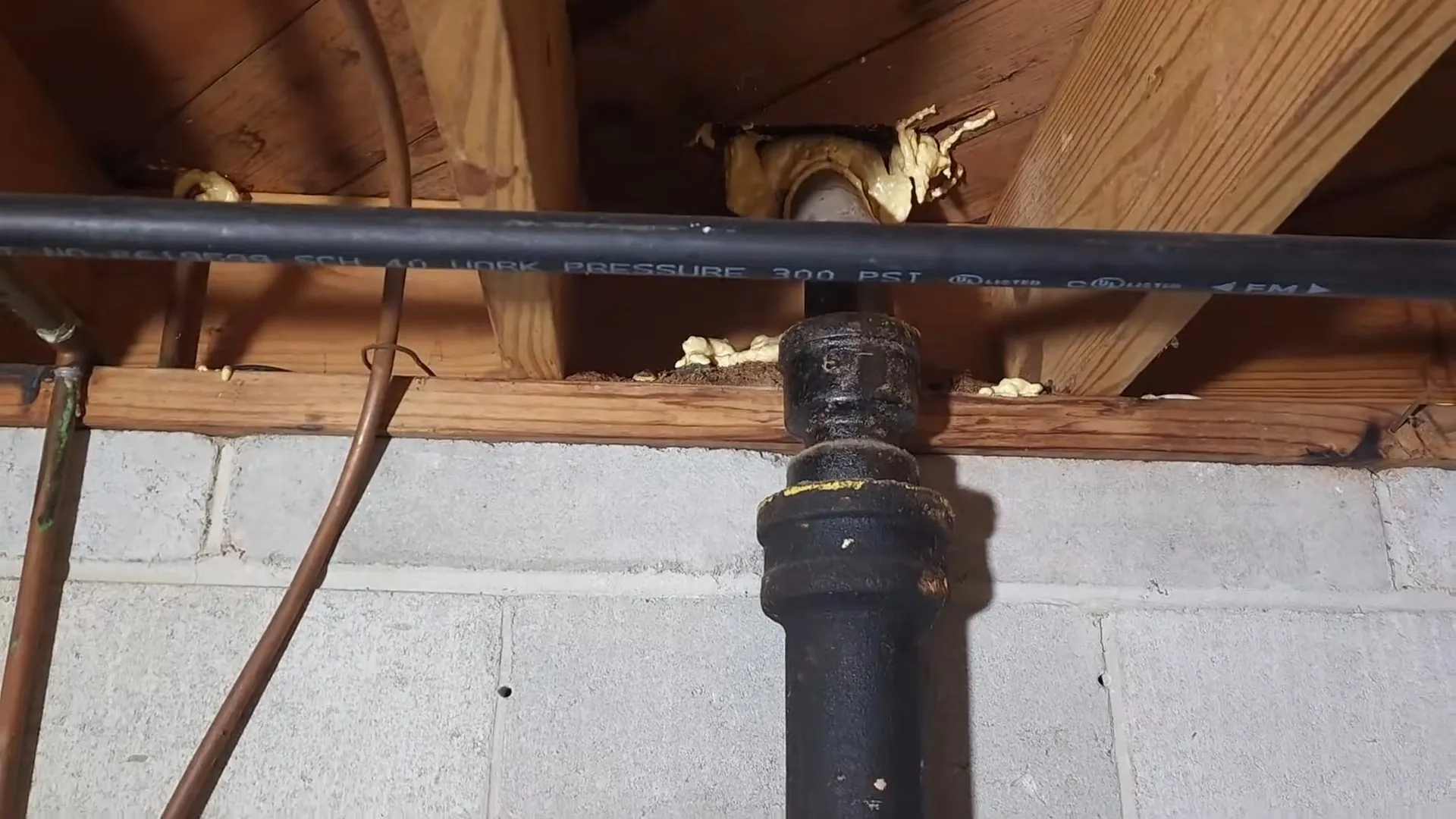 Black cast iron drain stack and a copper line under basement joists above a block wall