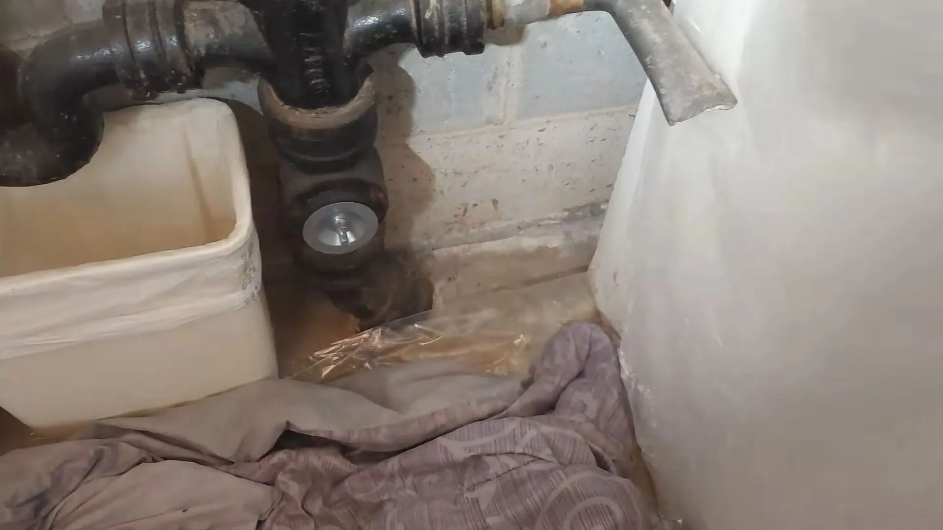 Black cast iron drain fittings joining at a floor opening beside a block wall