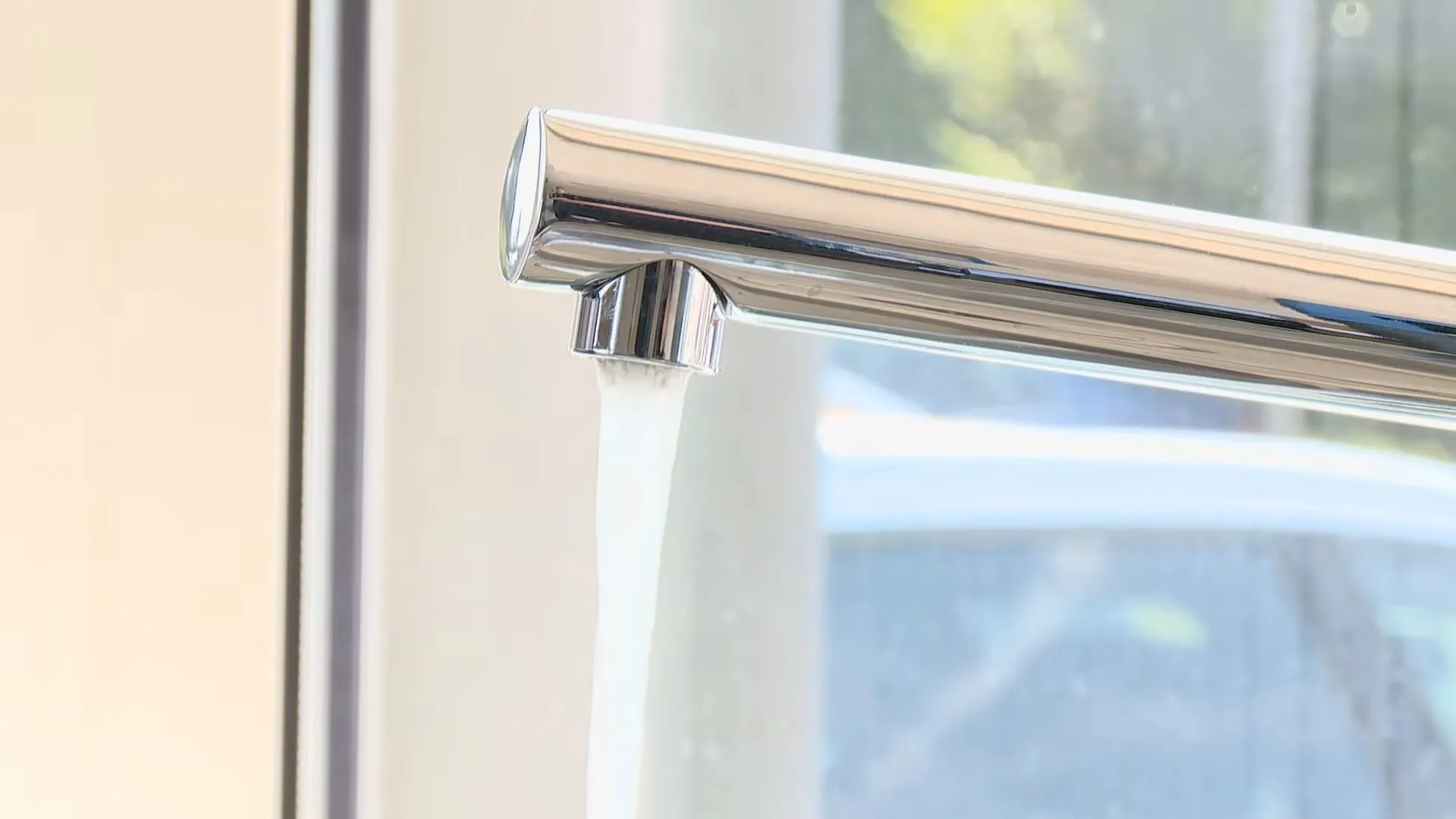 Chrome kitchen faucet running a steady stream of water beside a window