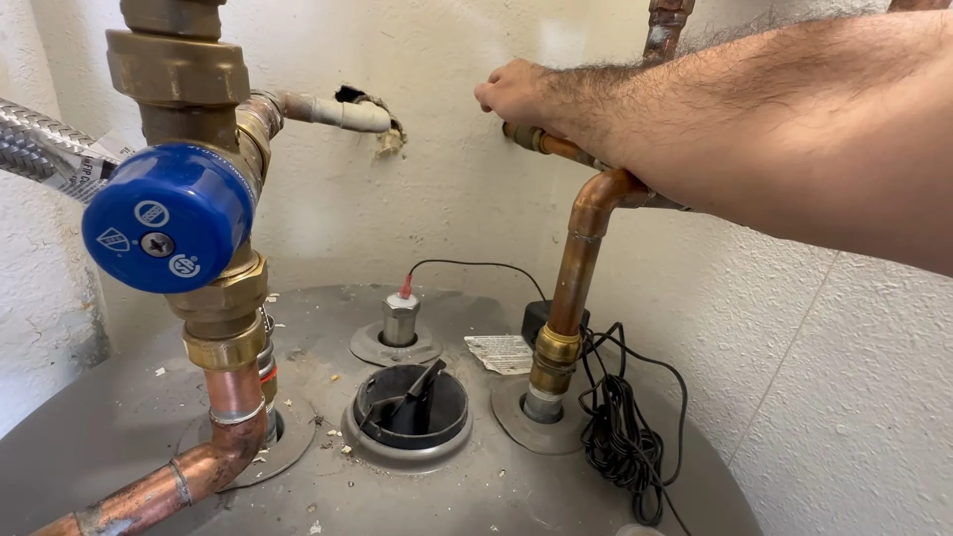 Hand on a copper outlet pipe at the top of a tank water heater with a blue valve on the inlet side