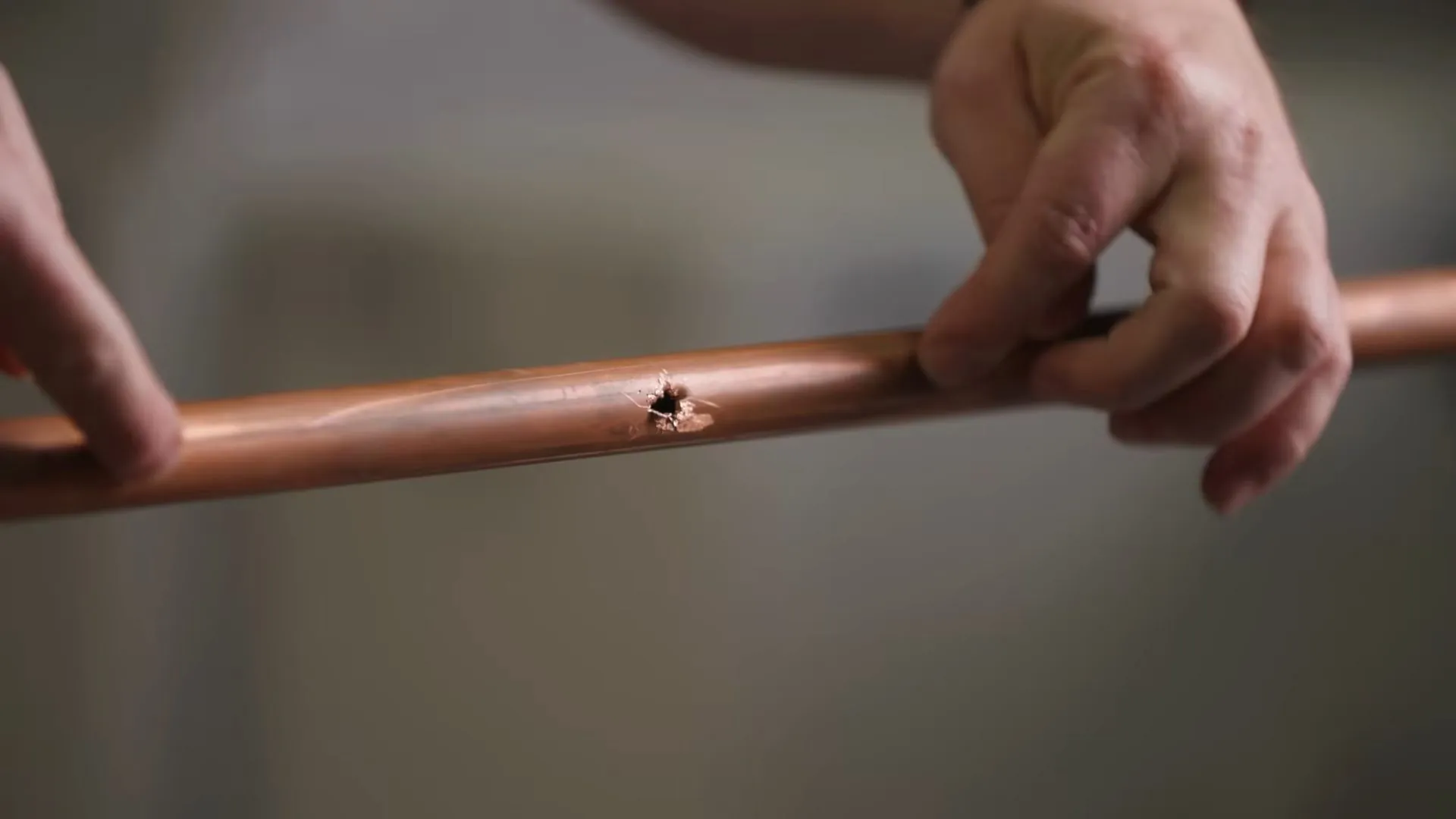 Hand holding a length of copper pipe with a small pinhole in the wall of the tube
