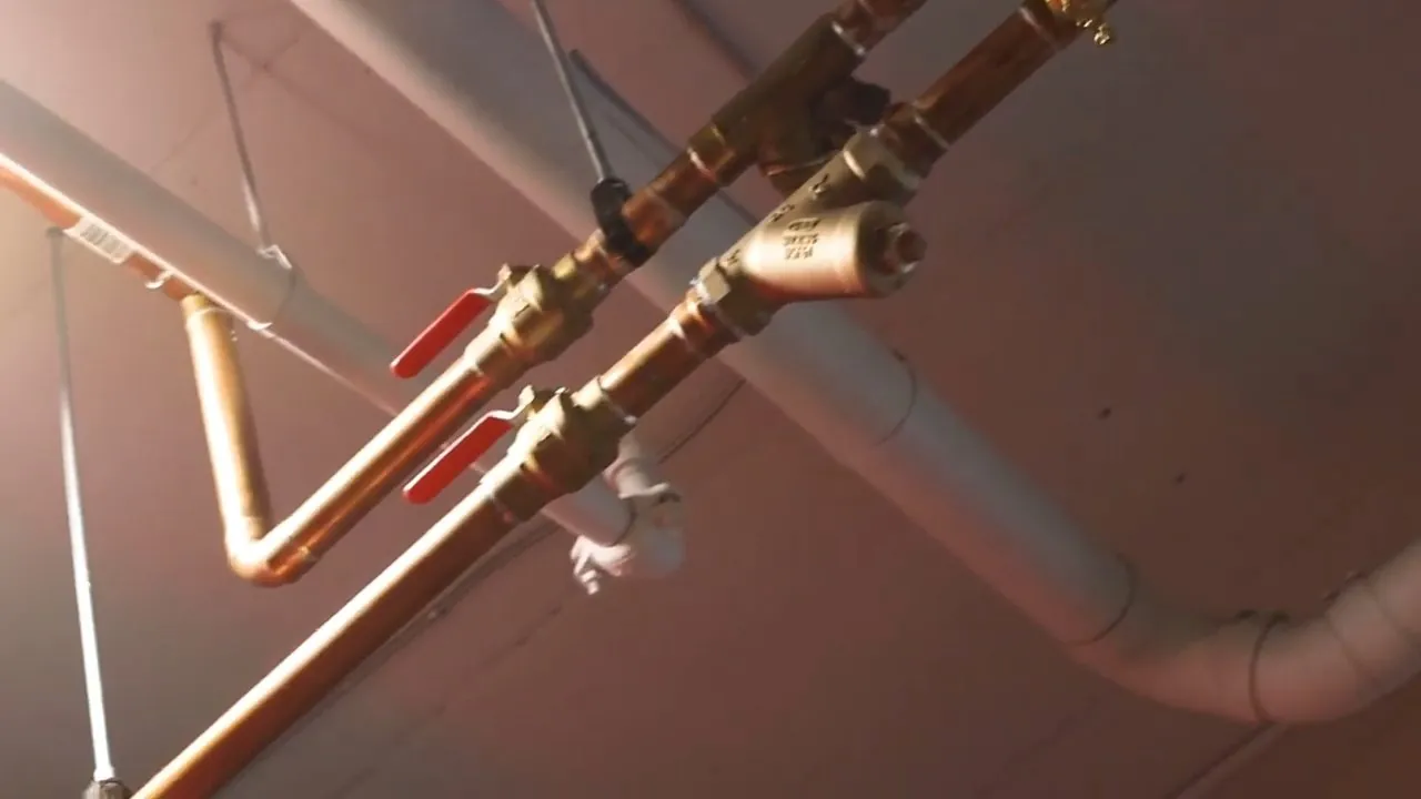 Copper pipes with red-handled brass valves and white drain pipe running along a ceiling
