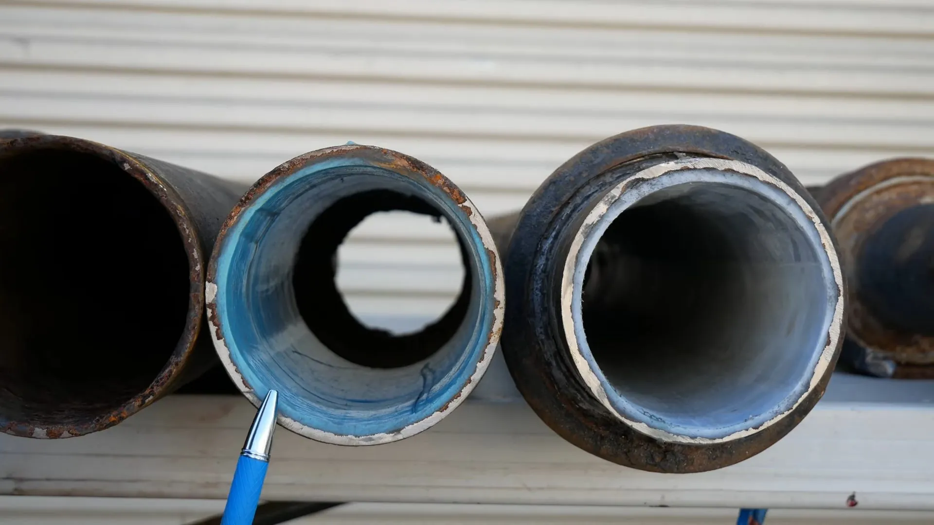 Three cut sections of sewer pipe with a blue liner visible inside two of them and a pen pointing at one