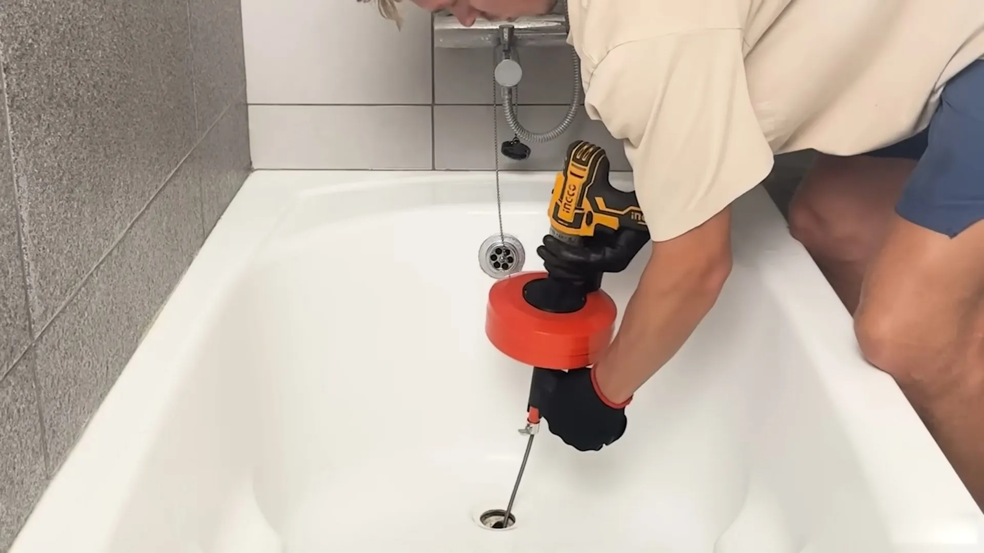 Hand-held drain snake being fed into a bathtub drain