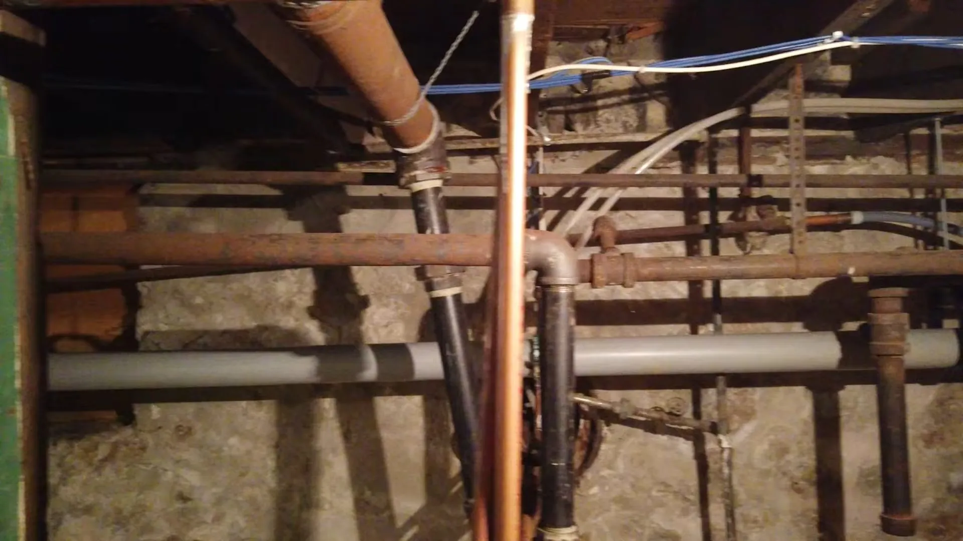 Exposed supply and drain lines running between basement joists