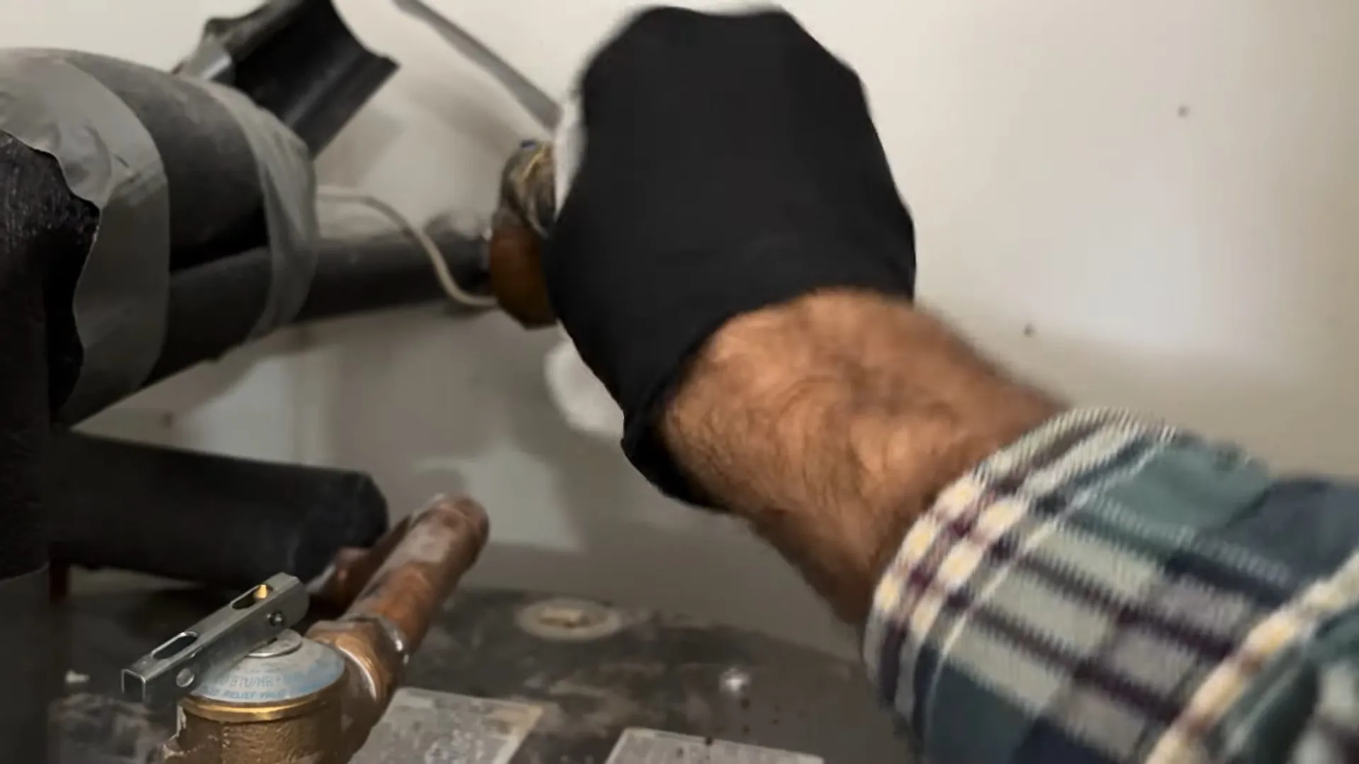 Gloved hand at a brass valve and copper fitting on a water heater