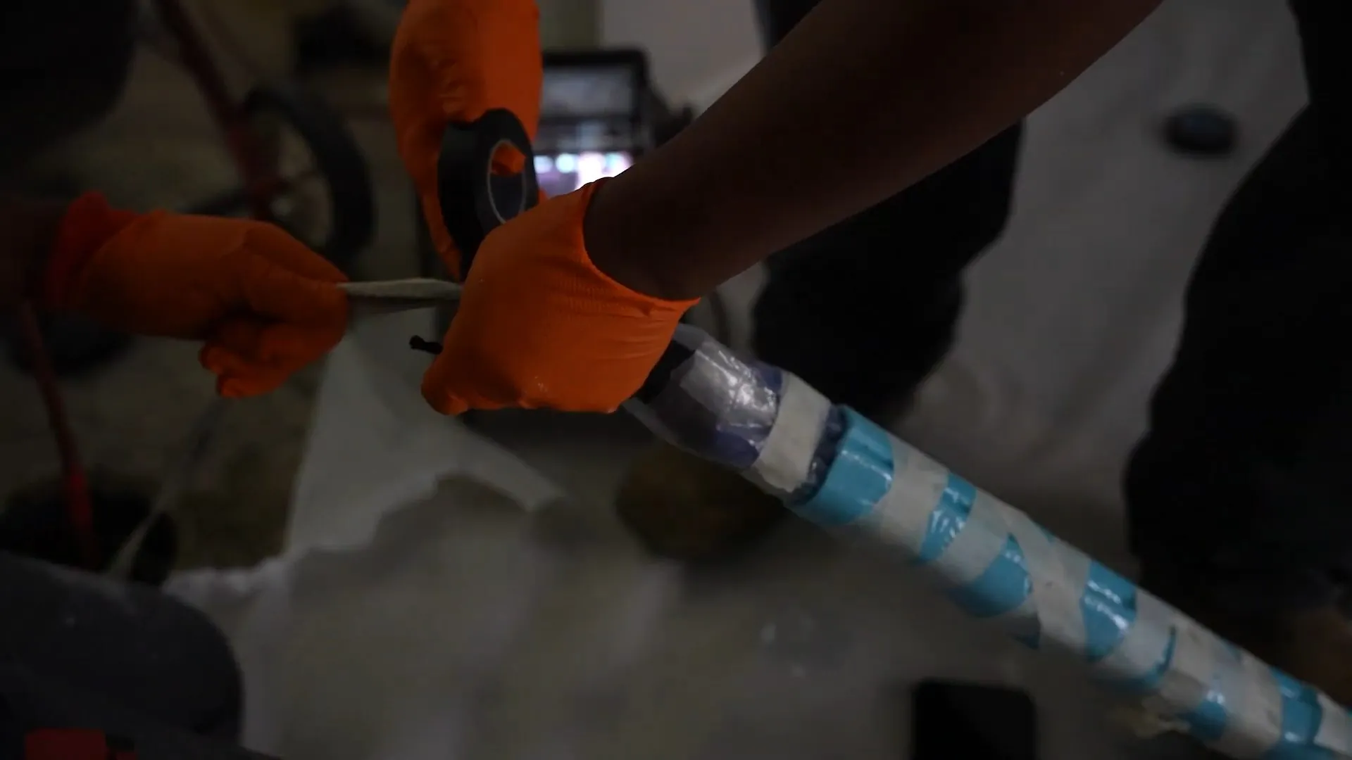 Gloved hands guiding a blue and white wrapped liner into a pipe opening