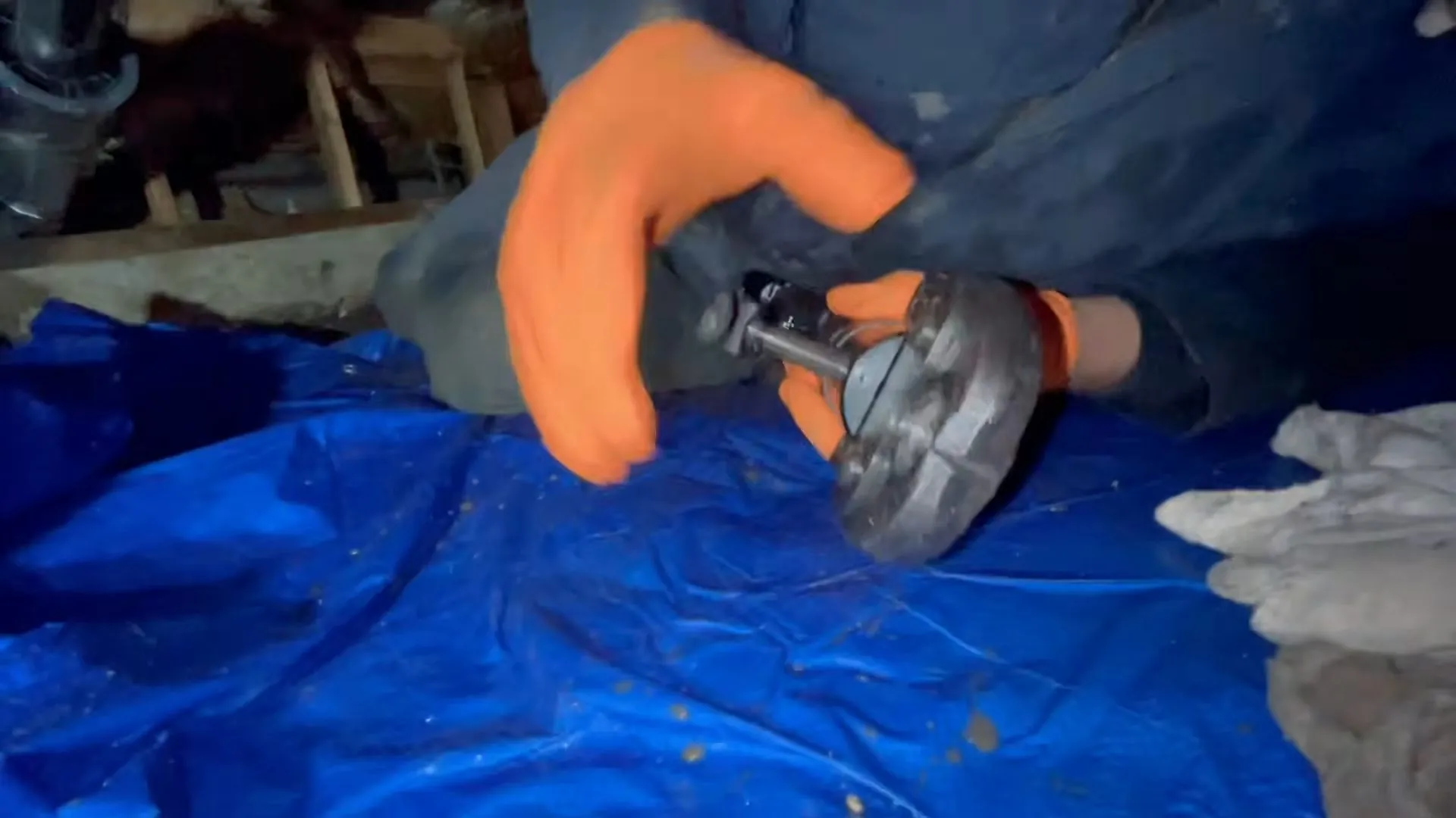 Gloved hands on a pipe fitting over a tarp in a crawlspace