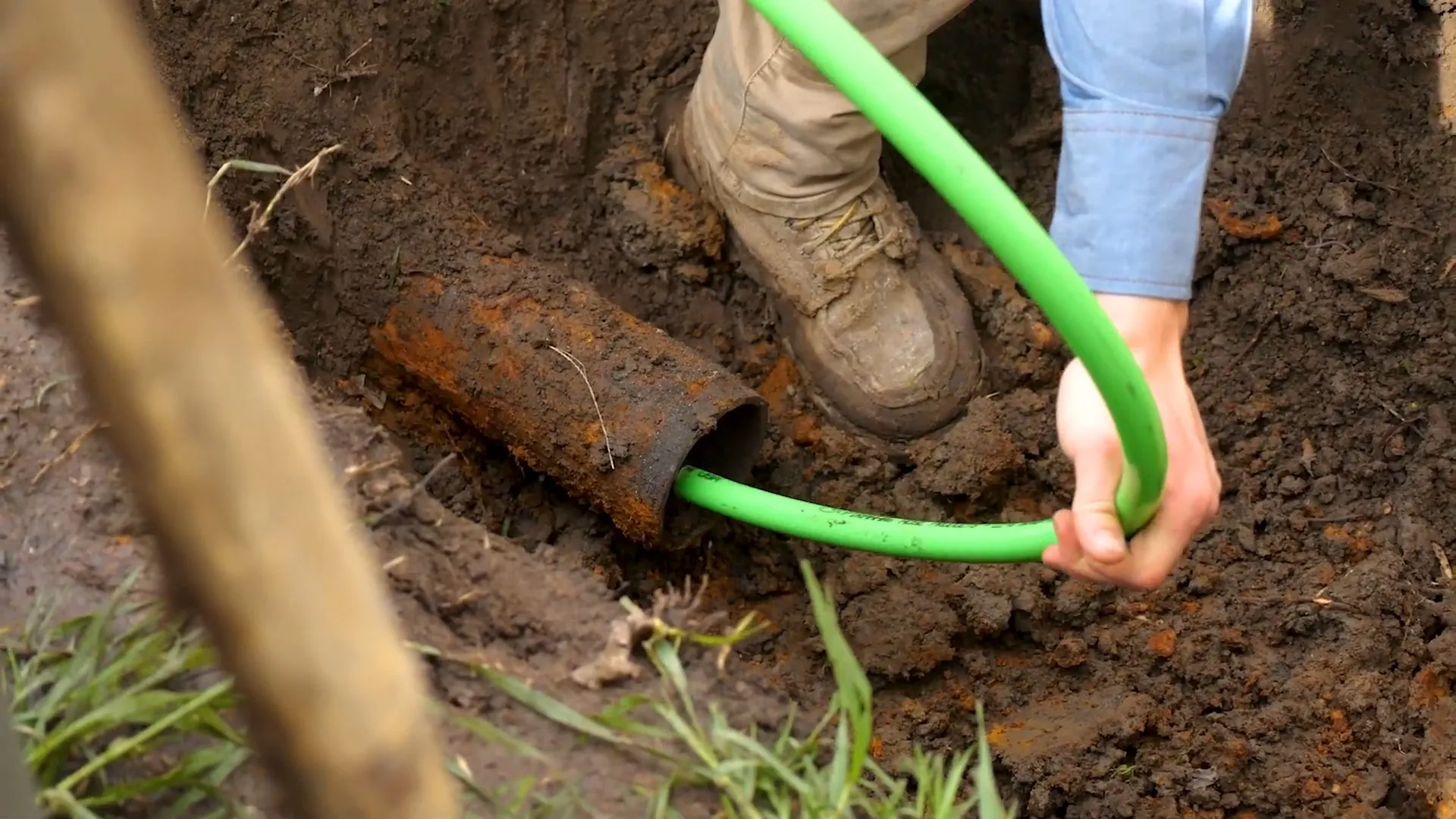 Green flexible liner tube being fed into an old rusted pipe in a dirt trench