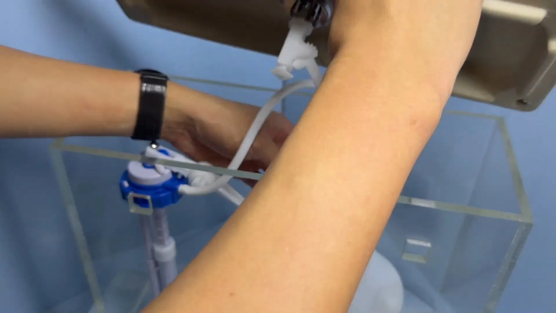 Hand adjusting the fill valve float inside a clear toilet tank