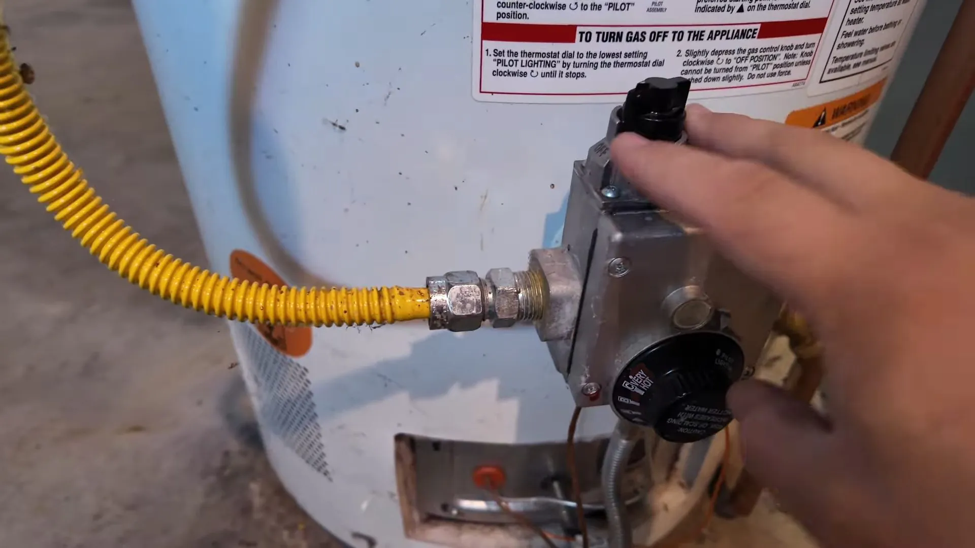 Hand on the gas control valve and yellow flex line of a water heater