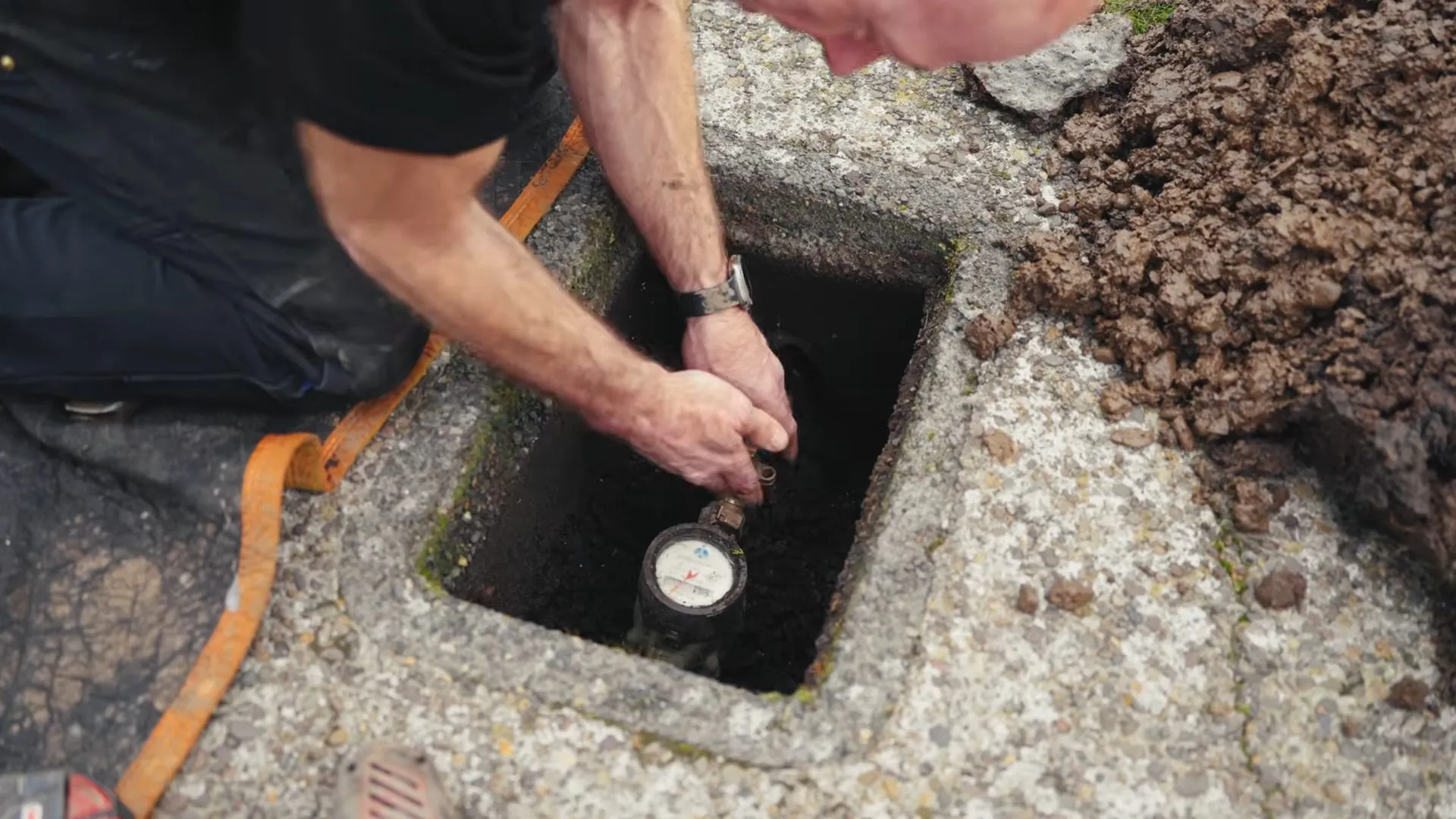 Hand reaching toward a water meter inside an open ground box