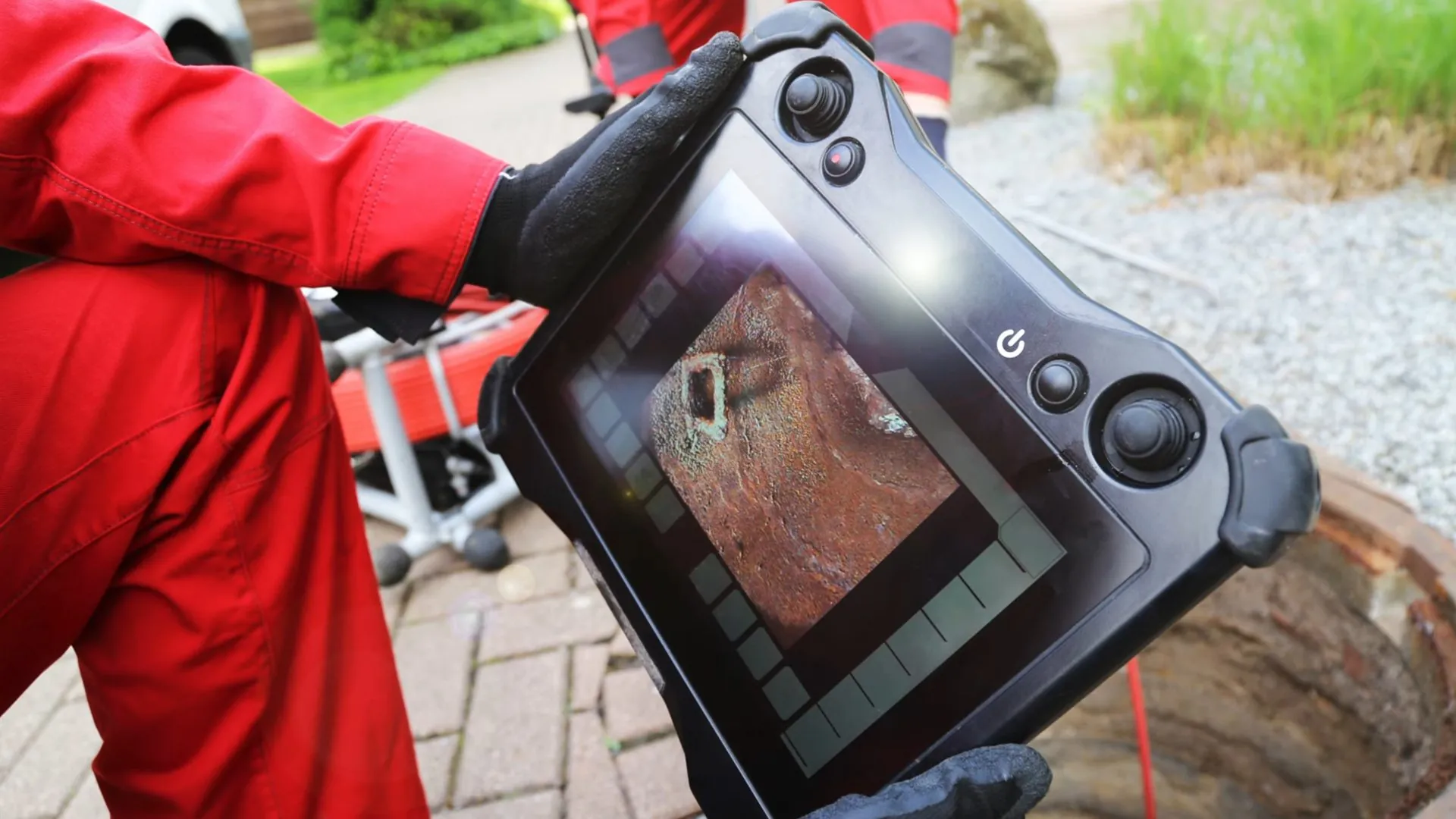 Hand-held camera monitor showing the inside of a pipe beside an open access