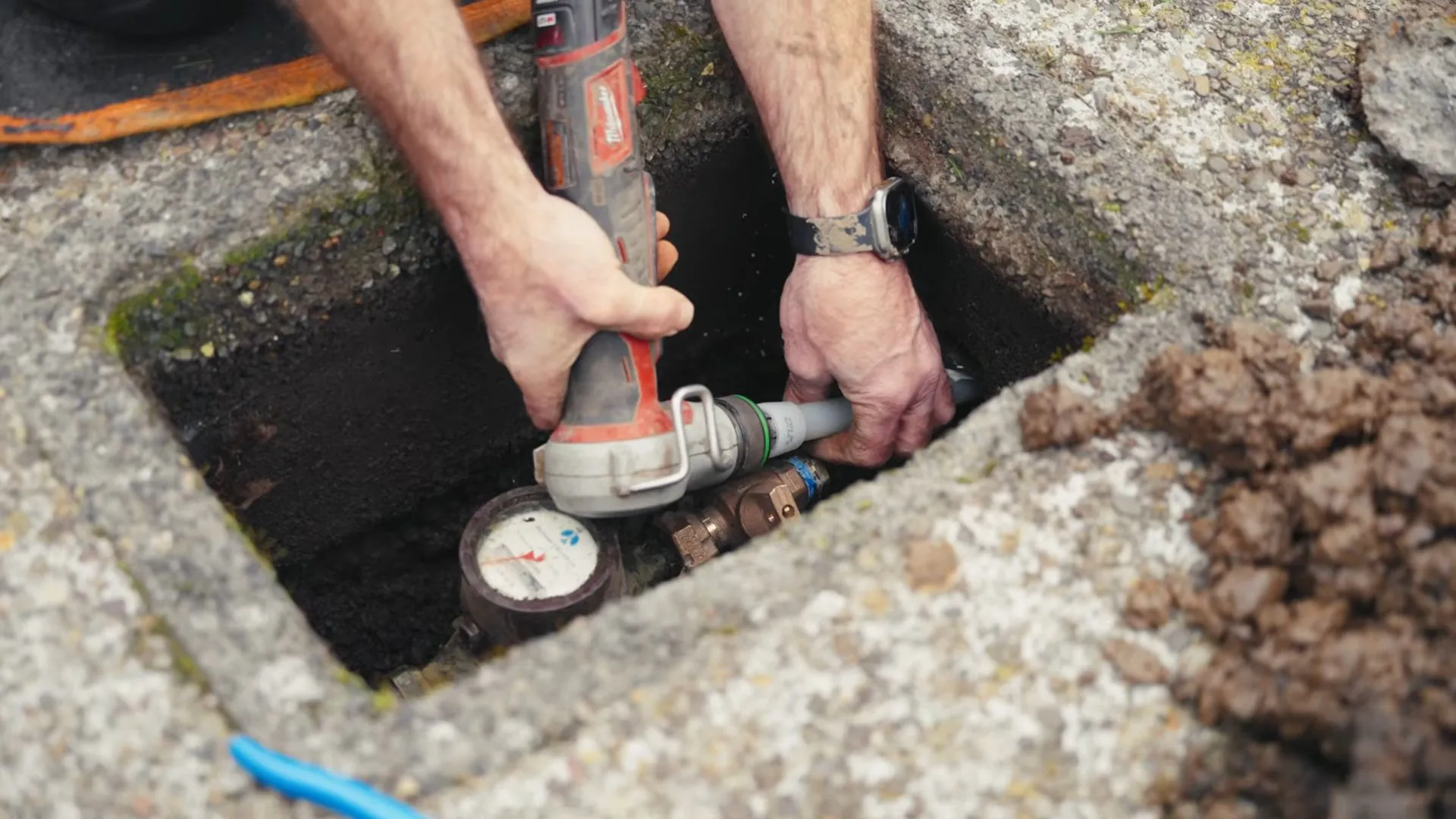 Hands working at a water meter and valve inside a ground box in a yard