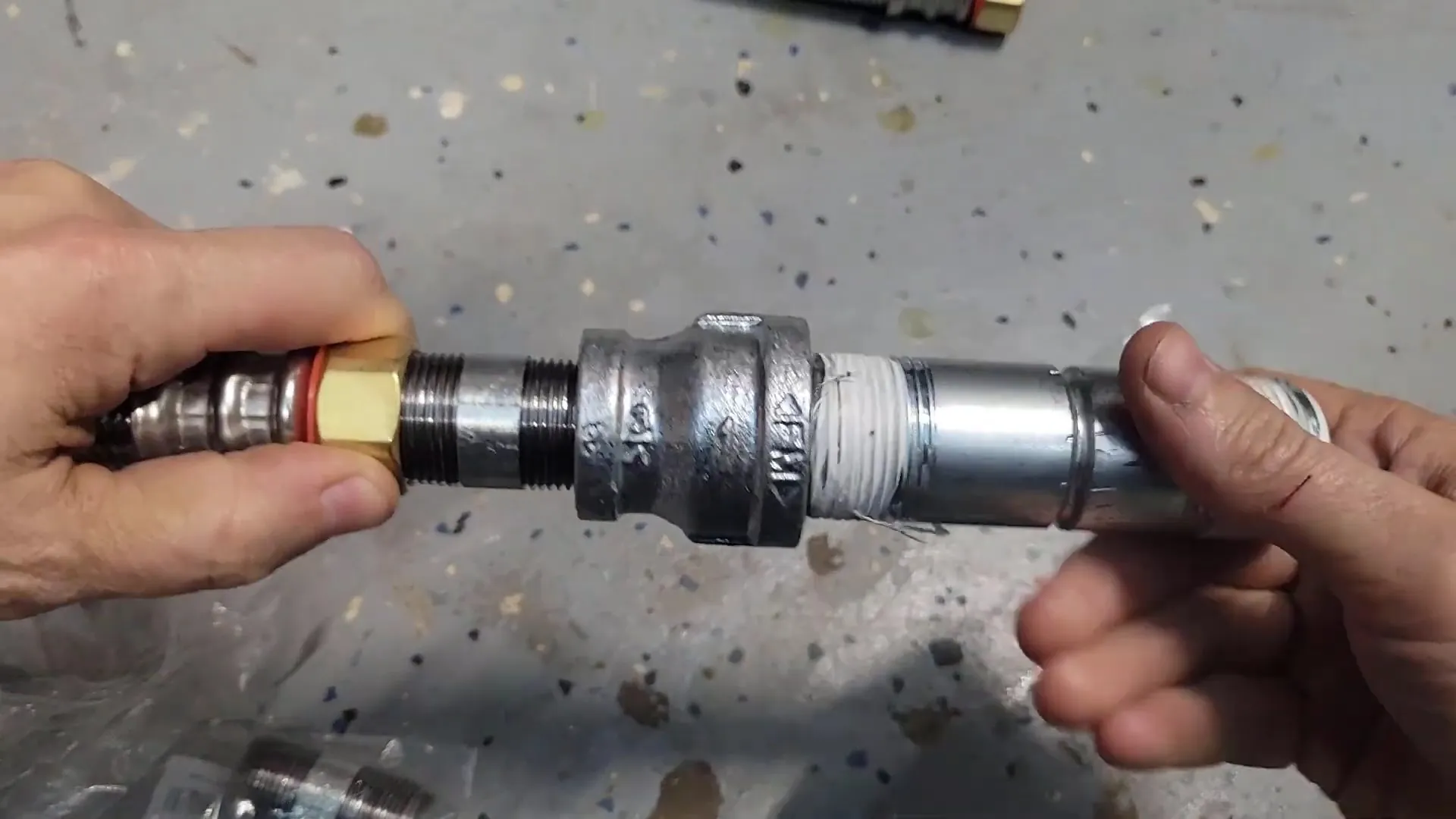 Two hands joining a galvanized threaded coupling to a flexible connector over a concrete floor