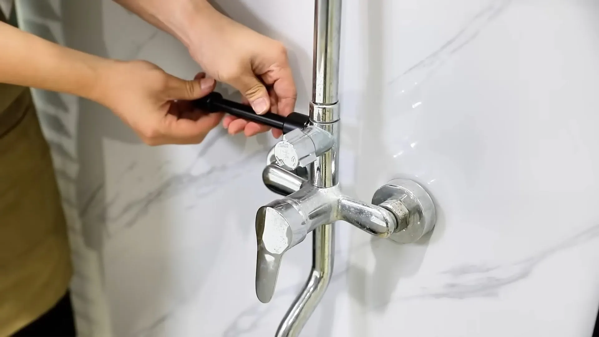 Hands working a tool at a chrome shower mixer valve