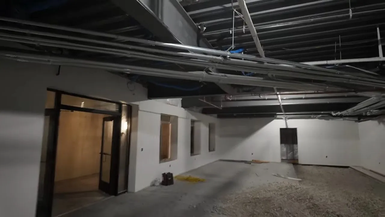 Open commercial space with bare ceiling pipes and a gravel floor before finishing