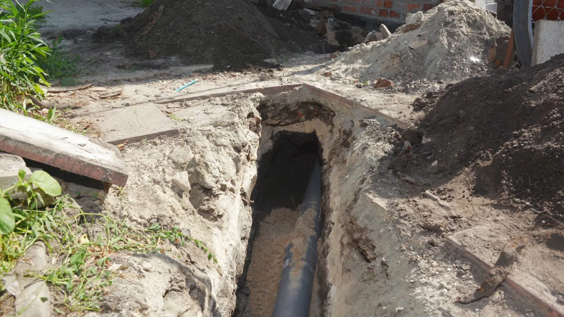 Open trench in a yard exposing a buried sewer pipe near a house