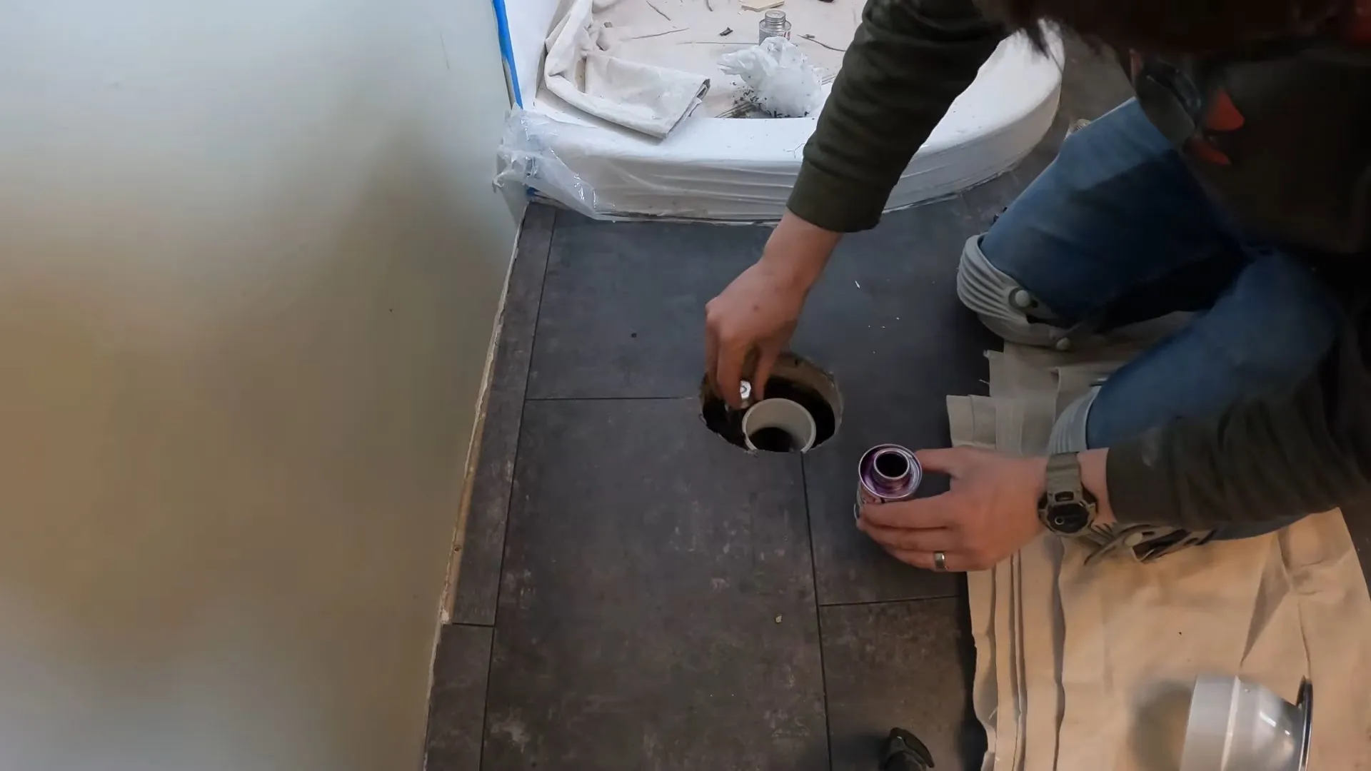 Person working at an open toilet flange on a tiled bathroom floor
