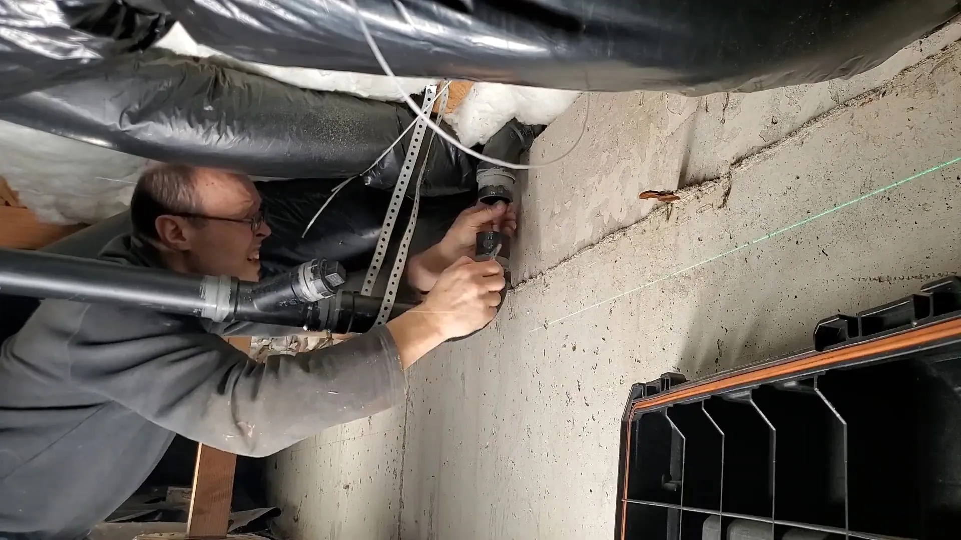 Plumber working on a drain connection beside a foundation wall under the floor