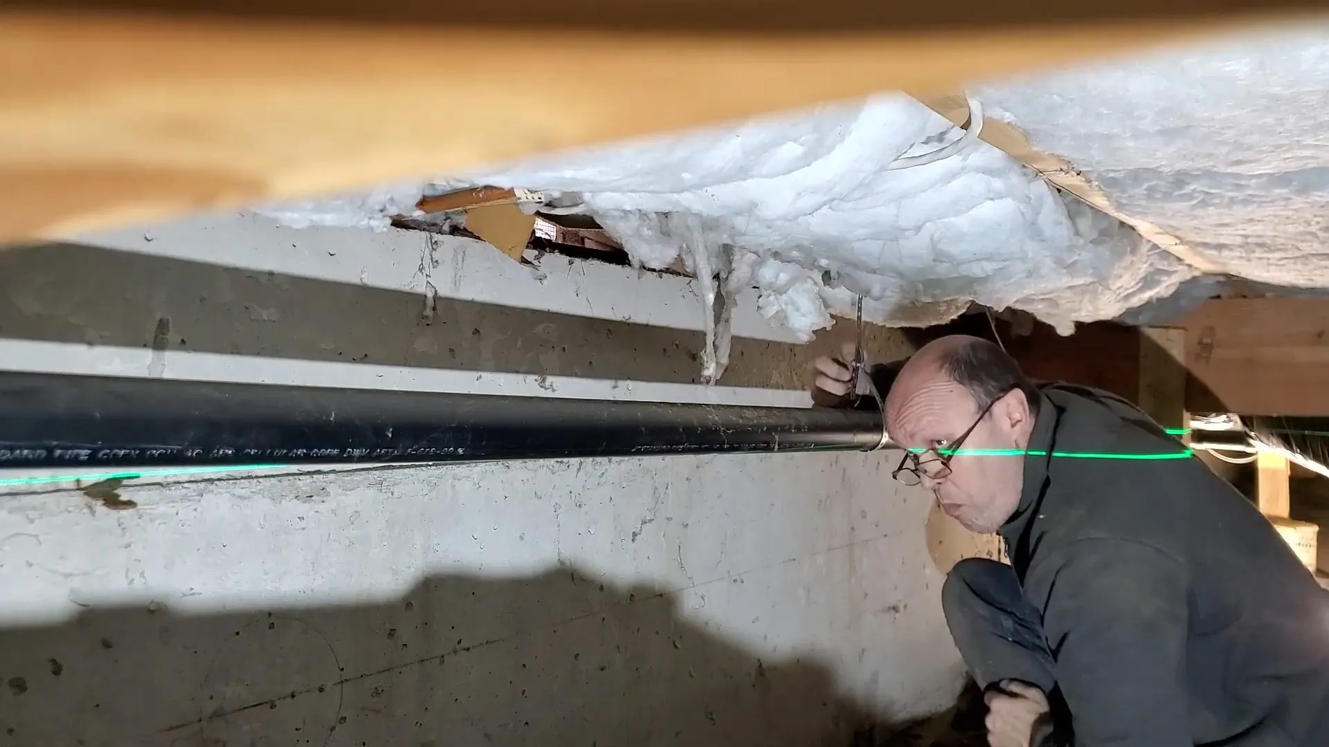 Plumber checking a pipe run in a crawlspace with a laser line