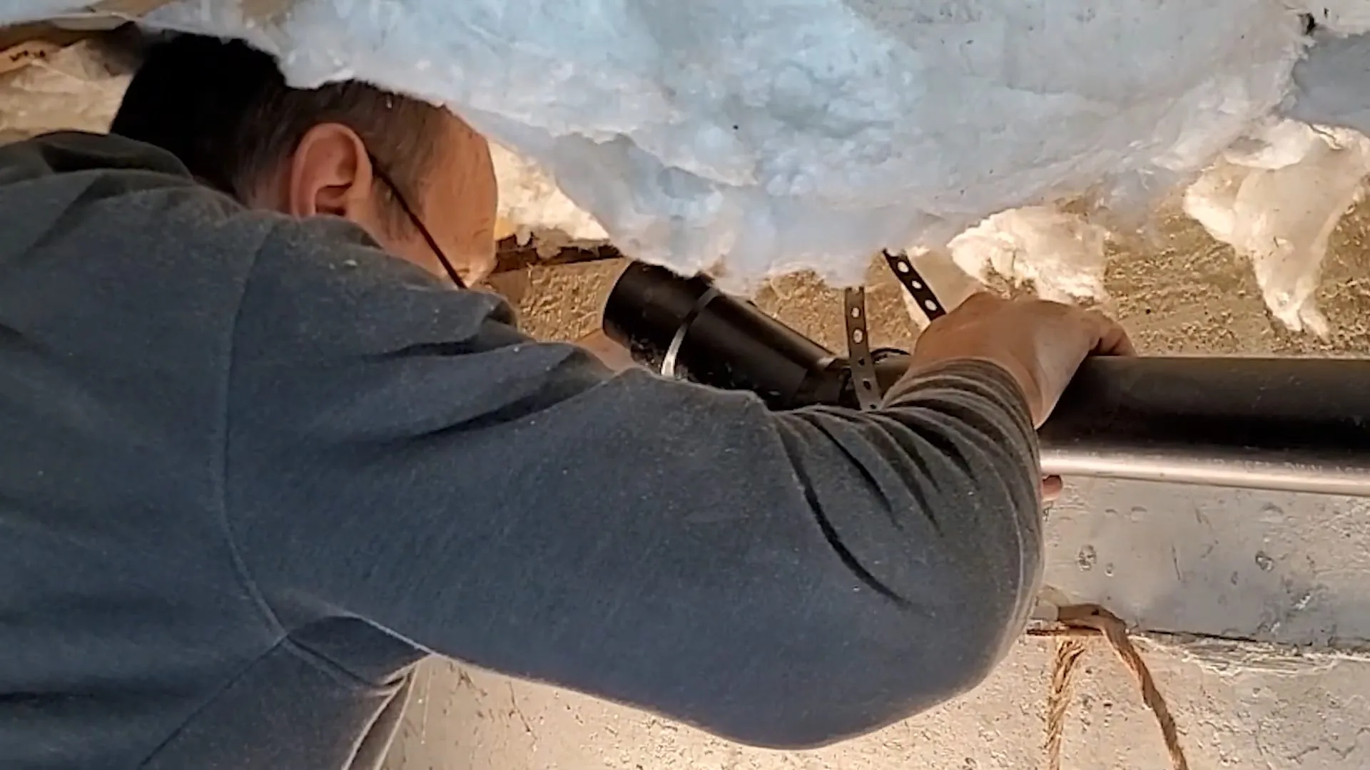 Plumber reaching up to a drain line under insulation in a crawlspace