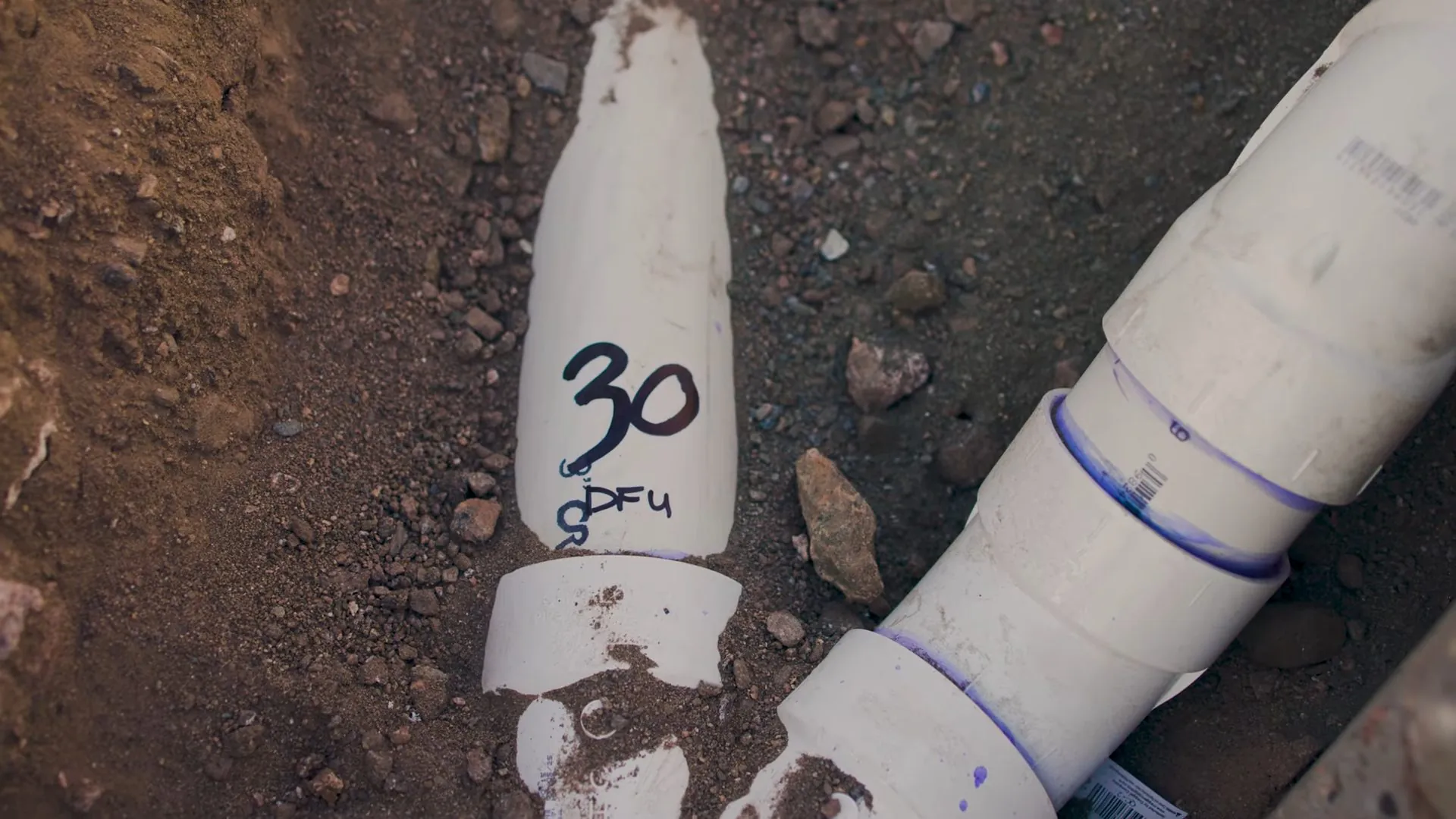 White PVC drain fittings in a dirt trench with a fixture count written in marker on one pipe