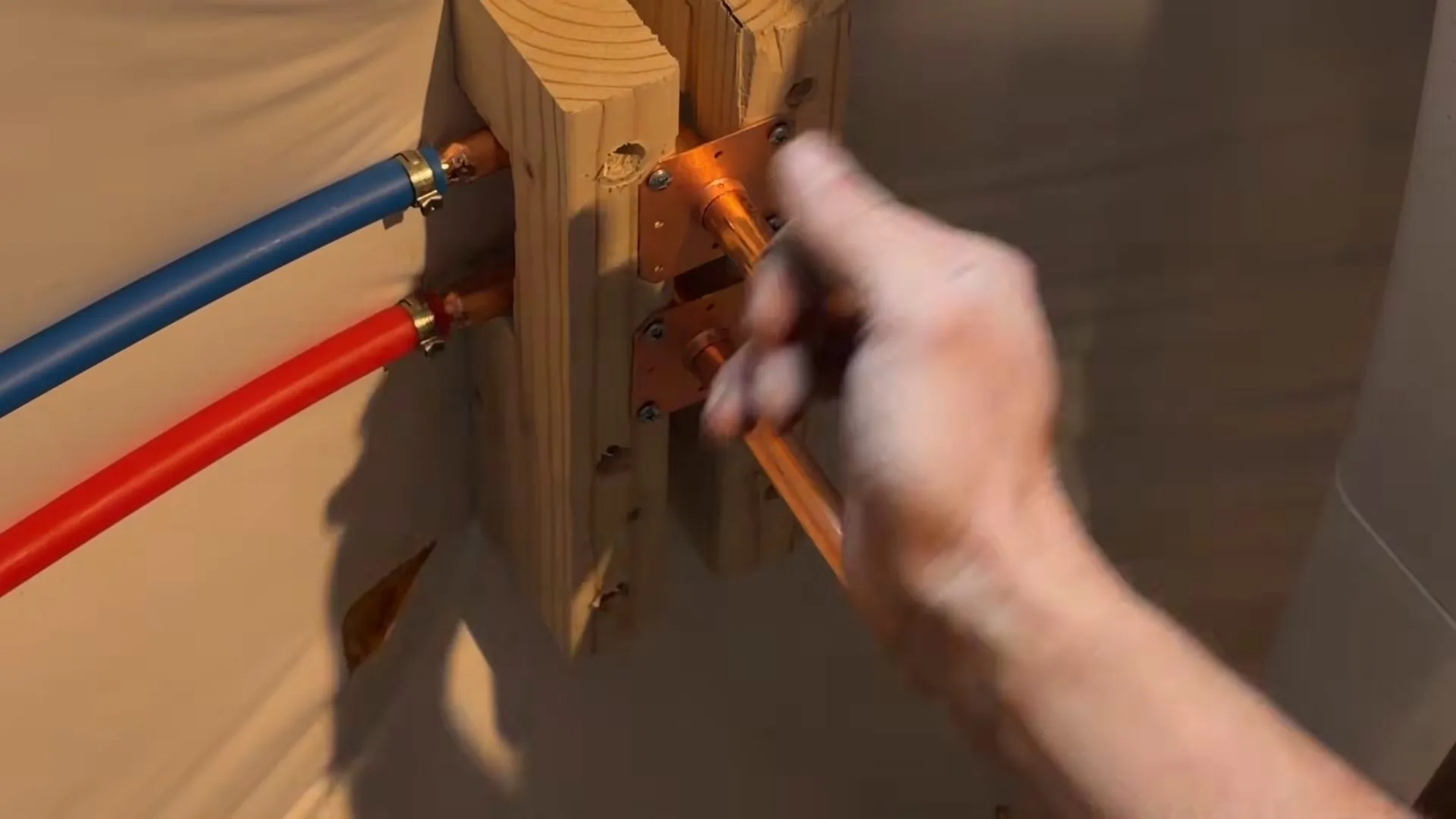 Red and blue PEX lines connected to copper stubs mounted on a wood block inside a wall
