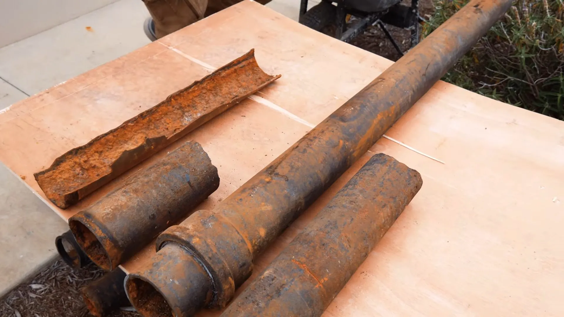 Rusted cast iron pipe sections laid on a plywood sheet, one split open lengthwise
