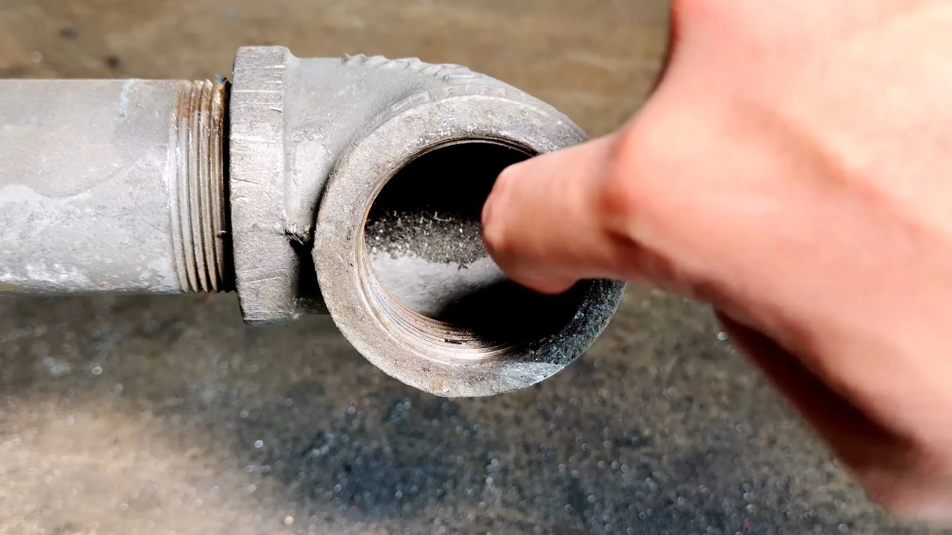 Close view of an old galvanized pipe elbow with scale built up inside