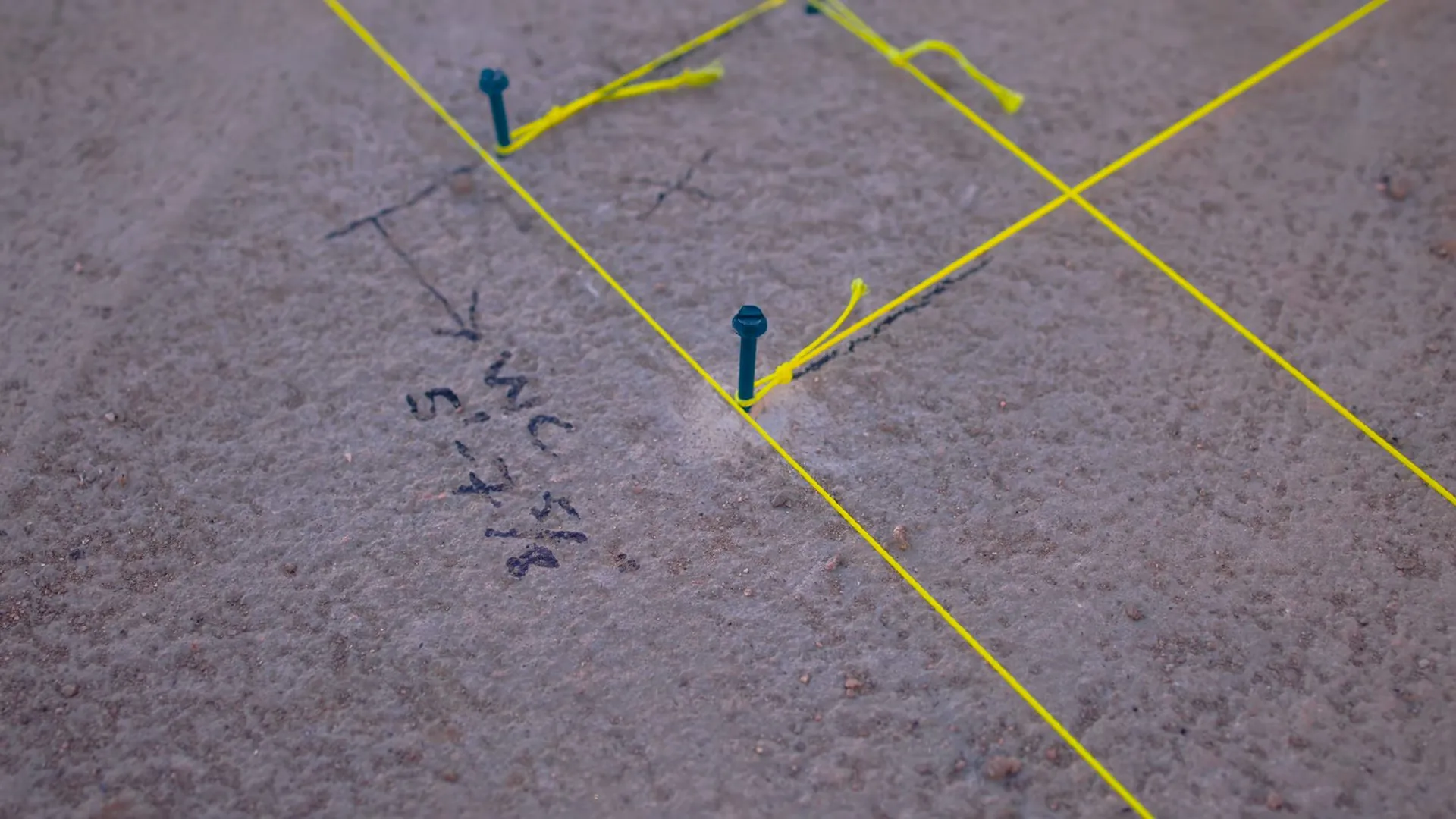 Concrete slab marked with string lines and notes showing a pipe route