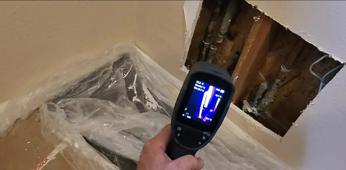 Thermal camera held toward an opened wall with pipes inside