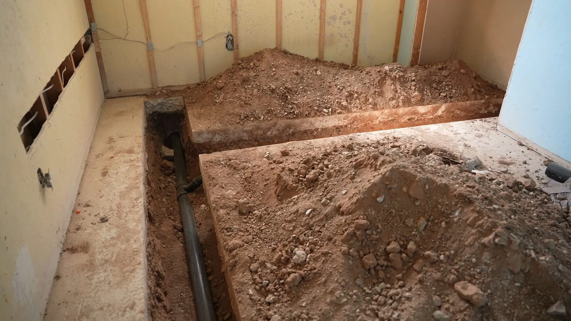 Trench cut through a basement floor with a drain line exposed