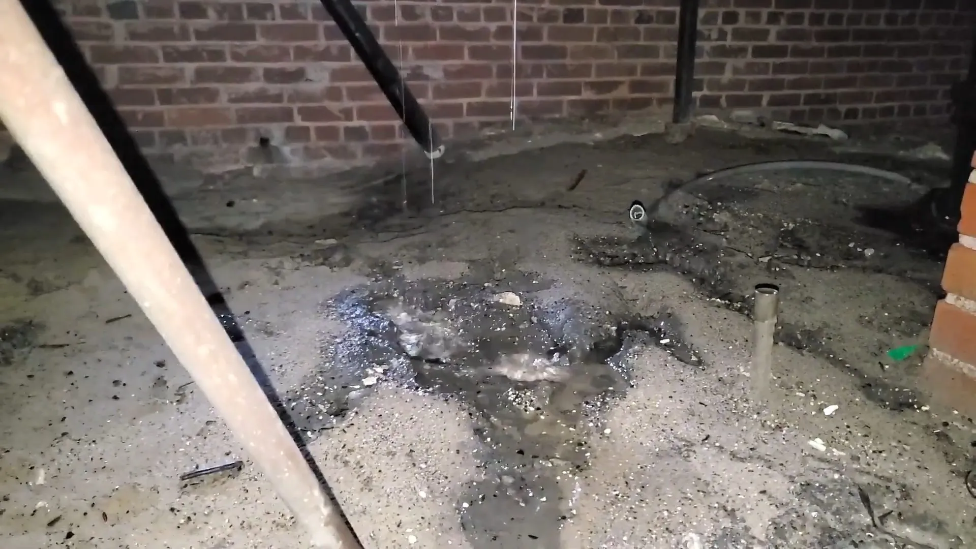 Wet debris covered ground under a dripping pipe in a crawlspace
